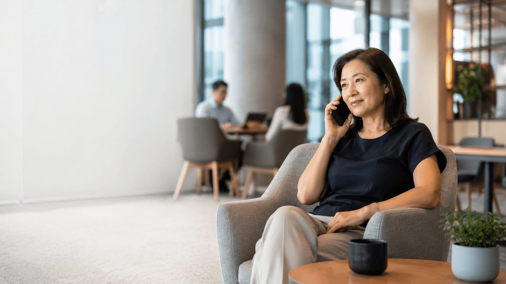 Mature Asian woman talking on a smartphone while sitting in a modern office lounge.